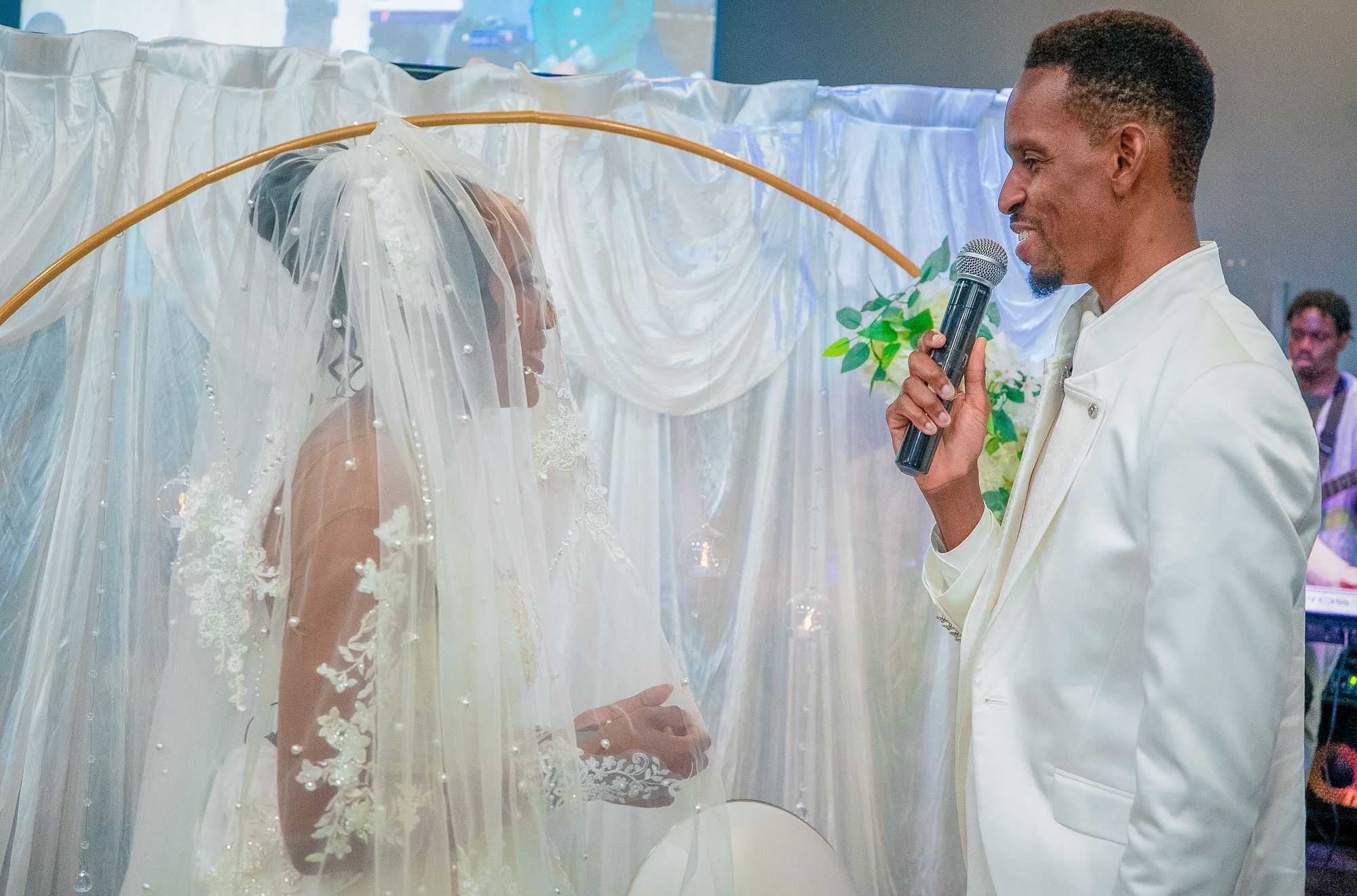 Le marié prend la parole, la mariée voilée devant l’arche dorée de la cérémonie