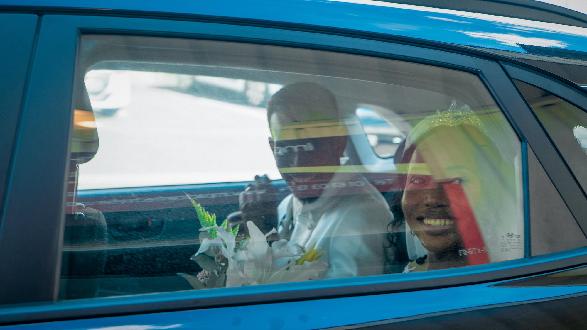 Les mariés dans la voiture, derrière la vitre, avec leur bouquet
